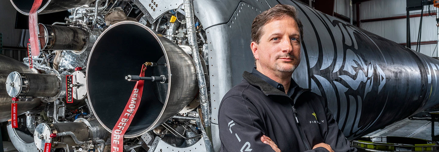 An aerospace engineer stands in front of a rocket booster