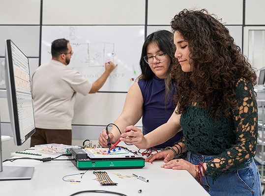 一人がラボでAnalog Discovery Studio Maxを使用し、もう一人がホワイトボードで問題を解決する様子