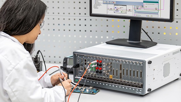 Engineer uses a PXI modular test system connected to a circuit board with probes to monitor results on a computer screen in a lab environment