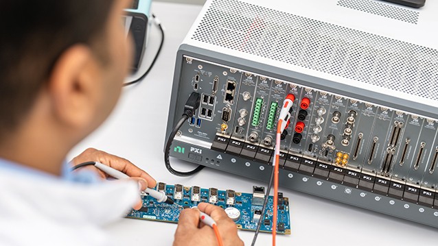 Person working with a PXI modular test system, probing a device under test on a lab bench.
