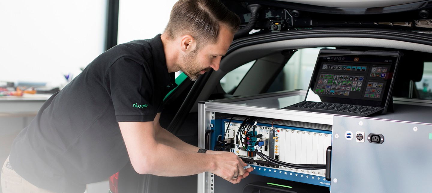 Mitarbeiter, der an einem NI PXI-basierten ADAS-Datensatzmesssystem im Kofferraum eines Fahrzeugs arbeitet