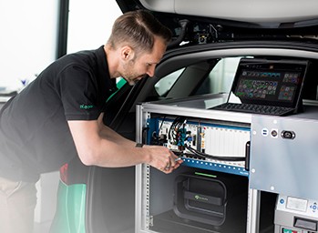 Mitarbeiter, der an einem NI PXI-basierten ADAS-Datensatzmesssystem im Kofferraum eines Fahrzeugs arbeitet