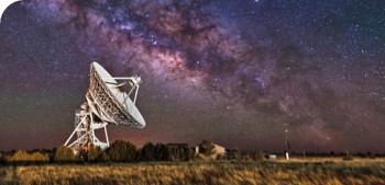 A radar antenna in a field points up at the night sky.