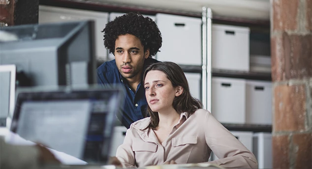 A man and a woman look at a monitor together.