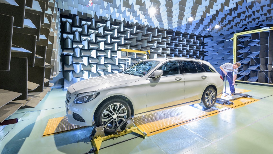 Un ingénieur de test effectue un test par dynamomètre sur une berline Mercedes blanche dans une chambre anéchoïque.