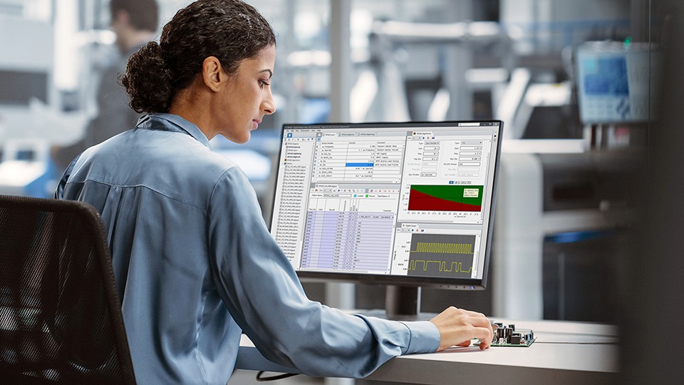 Production test engineer looking at two desktop computer monitors showing semiconductor device test plots.