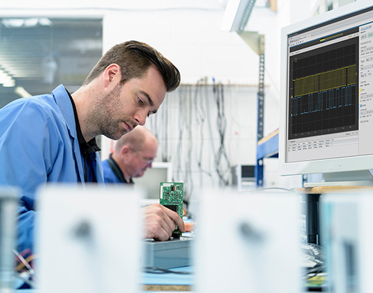 電子テスト機器と回路基板を用いて研究室の作業台で作業するエンジニア