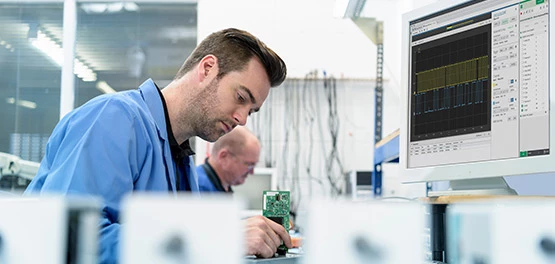 Engineer with a test module at hand and a monitor in front of him