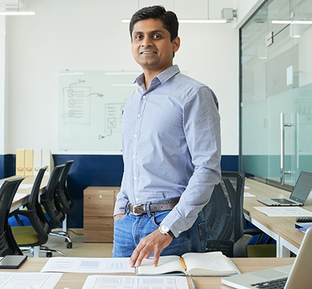 Ein Mann steht in einem Büro mit Notizen vor sich und Brainstorming-Aktivitäten auf der weißen Tafel hinter ihm
