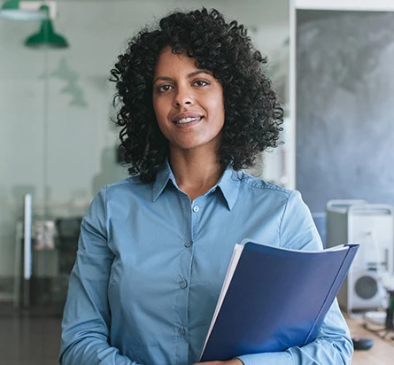 An NI partner is holding a portfolio of materials. She is smiling at the camera.