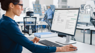 Engineer using NI TestStand on a desktop computer in a production test lab, building and monitoring automated test sequences to improve throughput, track results, and deploy tests across manufacturing systems.