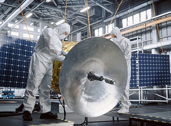 two engineers in a space suit testing satellite hardware