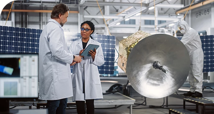 two engineers looking at satellite test data while a third engineer in a clean suit is inspecting the satellite hardware