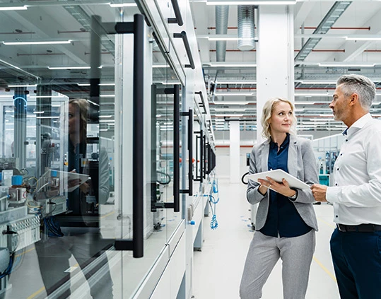 Businesswoman discussing Production Test with coworker at industrial machinery