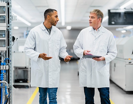 엔지니어들이 생산 테스터로 둘러싸인 제조 라인을 이동하며 테스트 결과를 검토합니다.