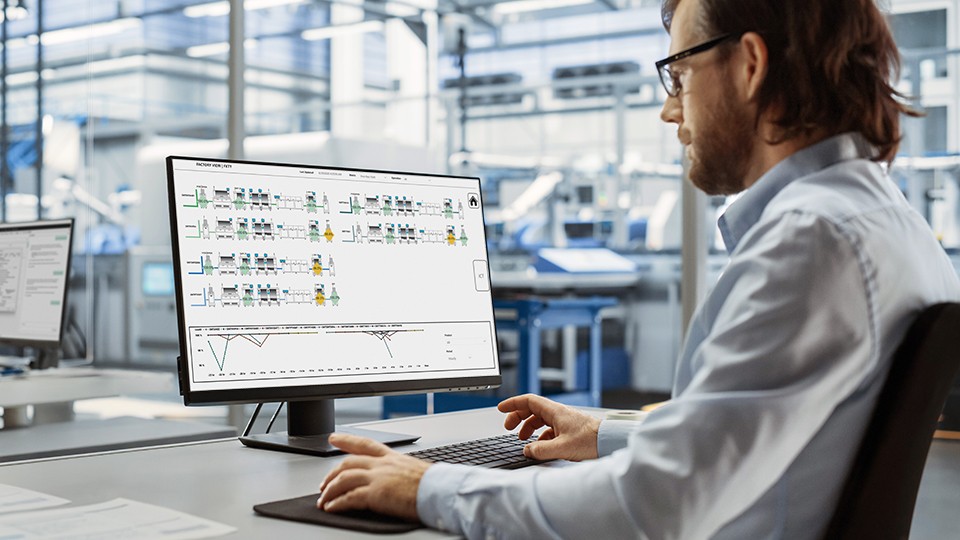 Automation engineer using desktop computer to monitor production process flow.