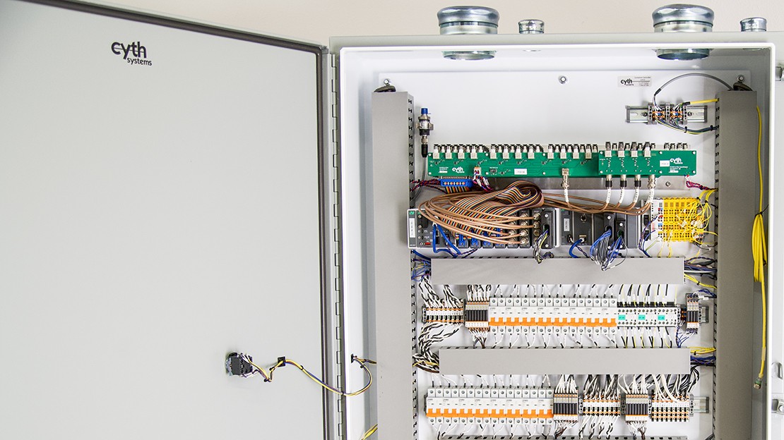 Open control panel showing rows of wired modules, terminal blocks, and circuit boards inside an industrial enclosure used for synchronized system control.