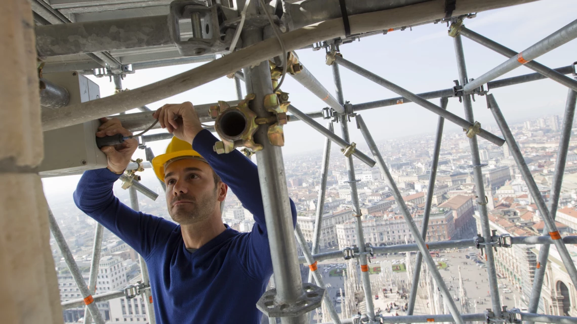 Un ingénieur portant un casque de sécurité assemble un système de test de déformation au-dessus d’un grand immeuble à Milan, en Italie.