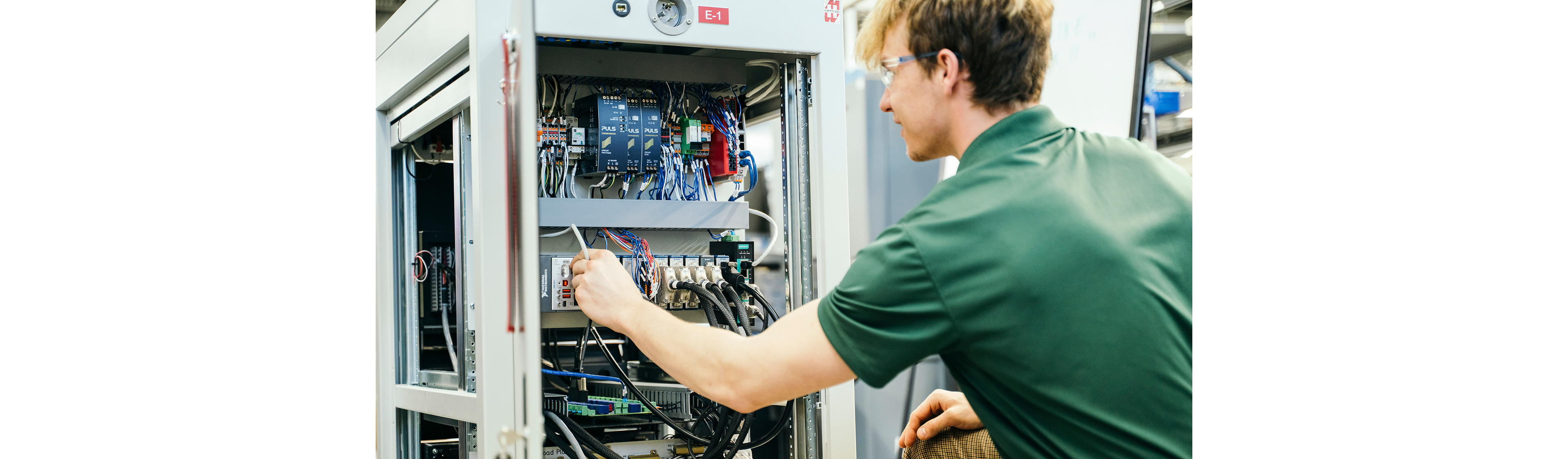 Techniker in Schutzbrillen, der Verbindungen in einem offenen elektrischen Schaltschrank prüft.