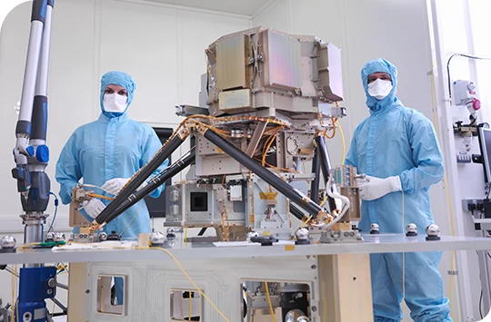 Dos ingenieros con trajes azules protectores trabajan en unidades reemplazables de línea en un satélite en un laboratorio