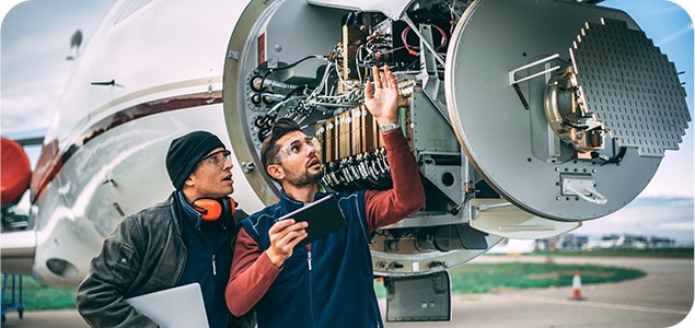 Engineers inspecting digital avionics on a radar component in the nose of an airplane