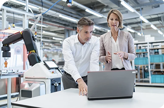 Two test managers in a factory assessing data on a laptop