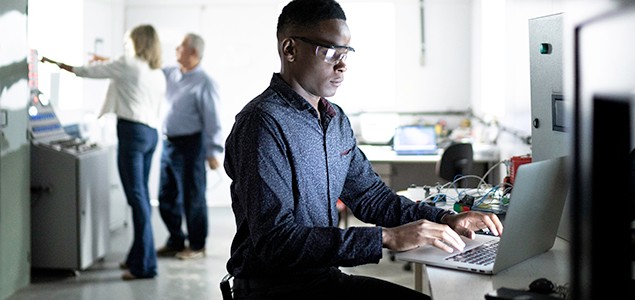 Un ingénieur travaillant sur un ordinateur avec une équipe en arrière-plan