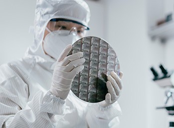 방진복을 입은 엔지니어가 반도체 웨이퍼를 검사합니다.