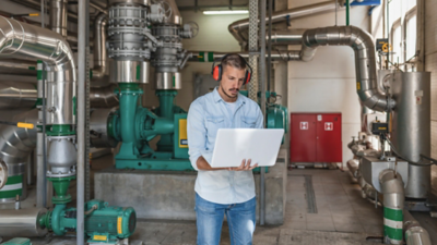 Maintenance Engineer is Monitoring the Boiling System at the Heating Plant. He is Standing Near the Power Generator with Protective Headphones.