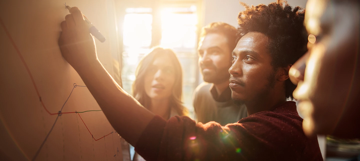  A team of engineers document their team's processes together on a whiteboard.