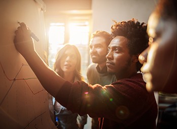 A team of engineers document their team's processes together on a whiteboard.