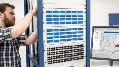 Engineer doing mechanical work on an NI HIL rig with a monitor showing NI’s HIL software VeriStand next to him.