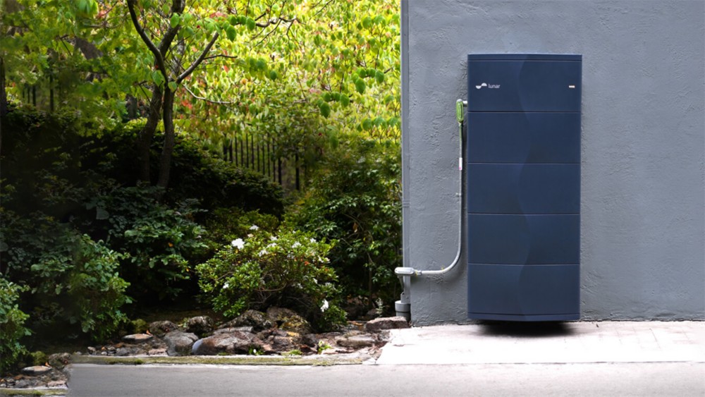Outdoor home energy storage battery installed beside a house, surrounded by greenery.