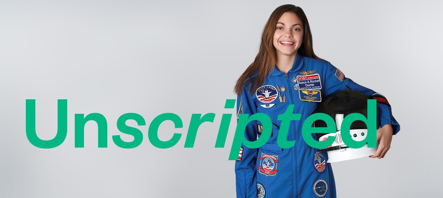 Future astronaut Alyssa Carson appears in blue flight suit behind green NI Unscripted logo. She is holding a helmet.
