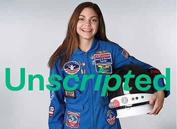 Future astronaut Alyssa Carson appears in blue flight suit behind green NI Unscripted logo. She is holding a helmet.