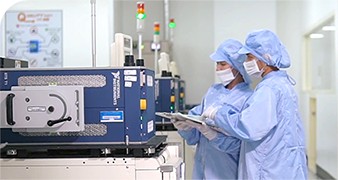 Two engineers in scrubs, hairnets, and masks run a production test