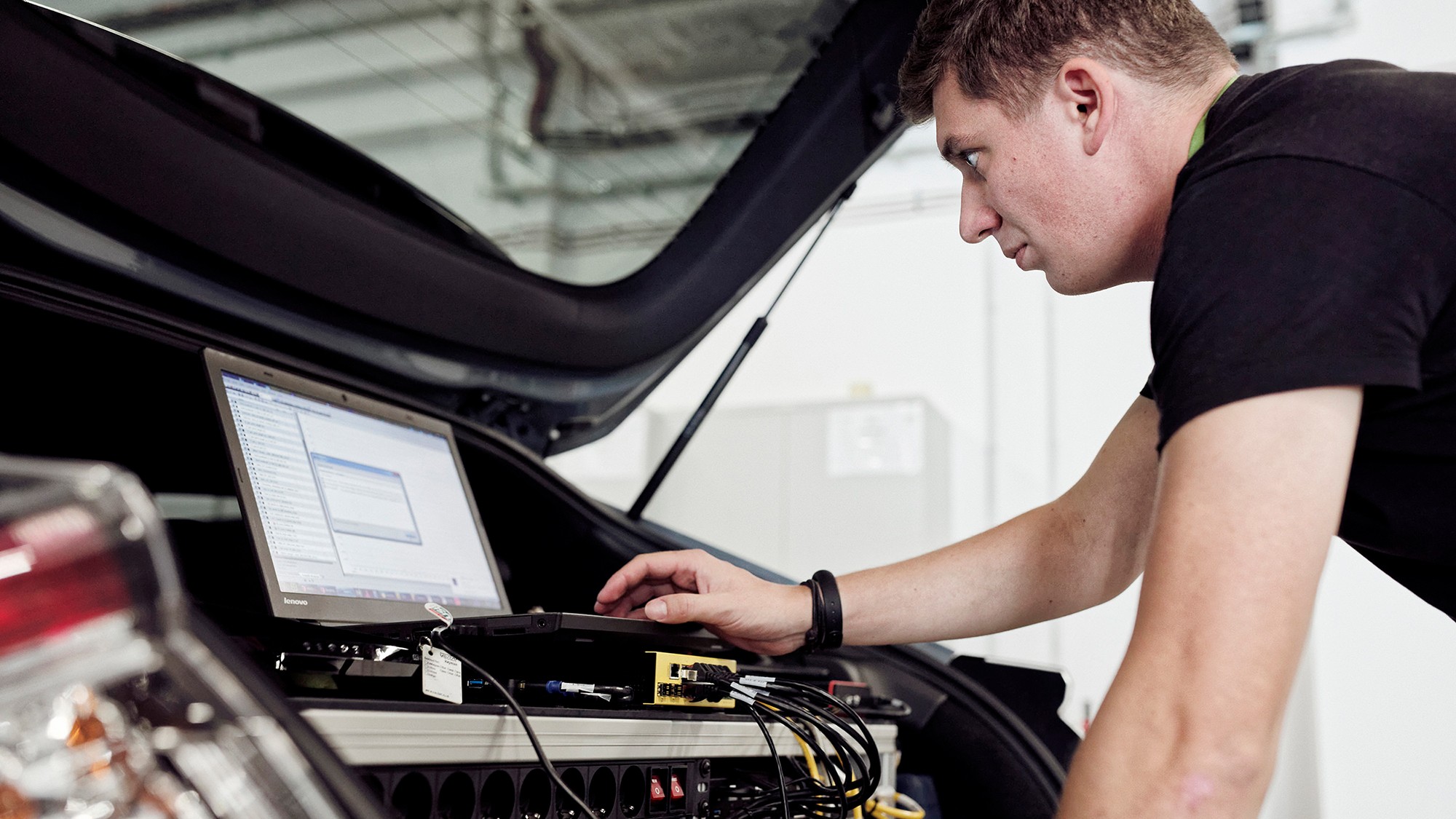 Engineer works on a laptop connected to electronic testing equipment installed in the cargo area of a vehicle.