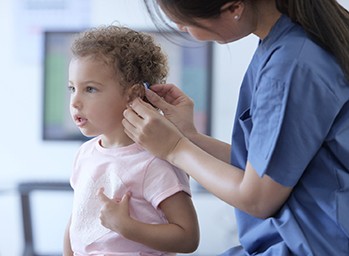 A doctor fits a young girl with a hearing device containing a small, long-lasting battery.