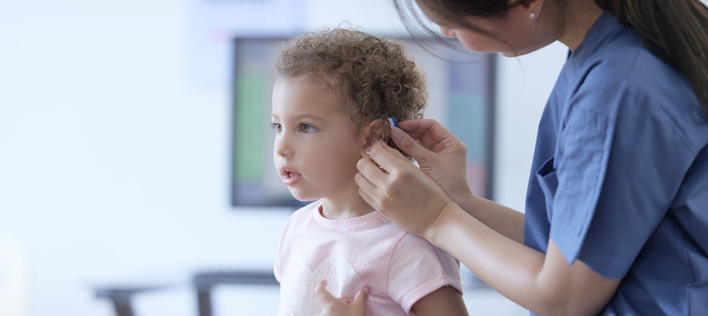 A doctor fits a young girl with a hearing device containing a small, long-lasting battery.