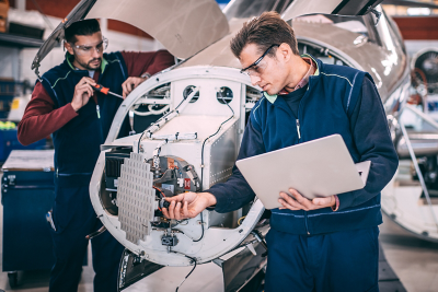 Two engineers perform an inspection and operational test of an aircraft engine and avionics sensor cluster.