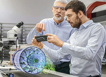 Two engineers work with mobile phone using augmented reality holographic projection 3D model of the engine turbine prototype. Development of virtual mixed reality application.